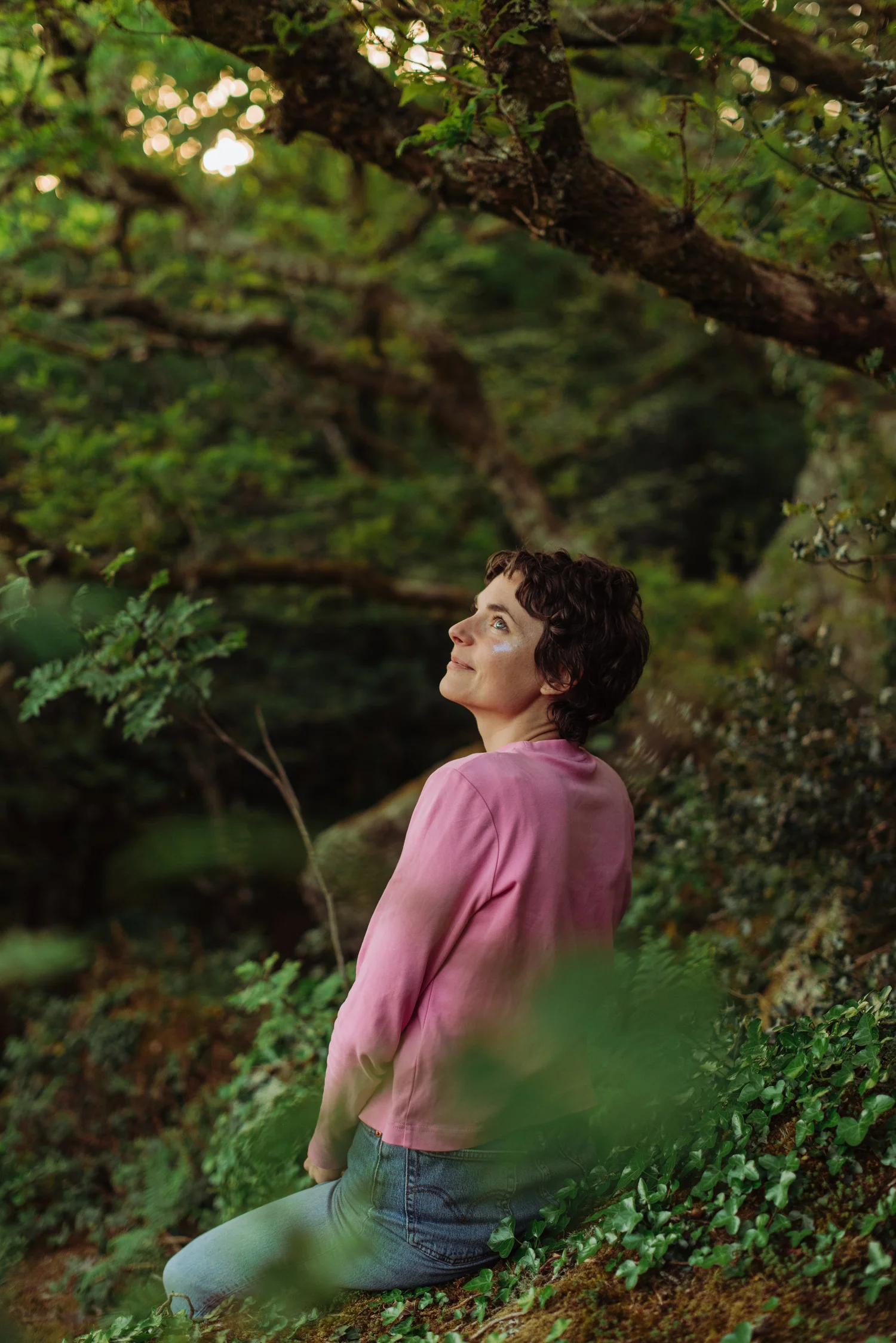 Becky Rui, personal brand photographer, sitting in mossy Devon woodland and looking up through the trees